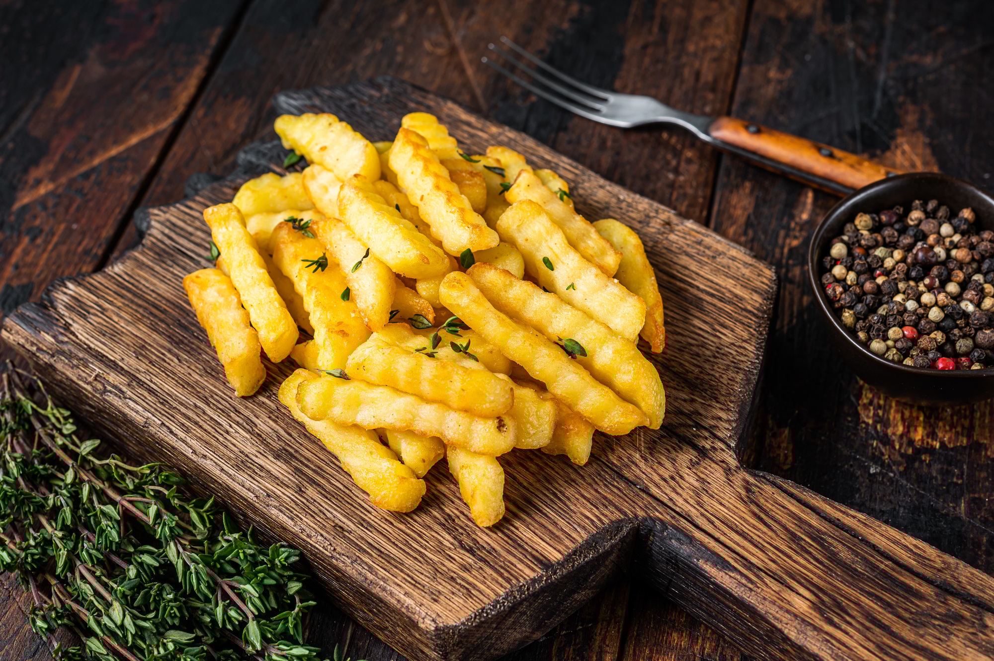 Baked Crinkle French fries potatoes sticks or chips on a wooden board.