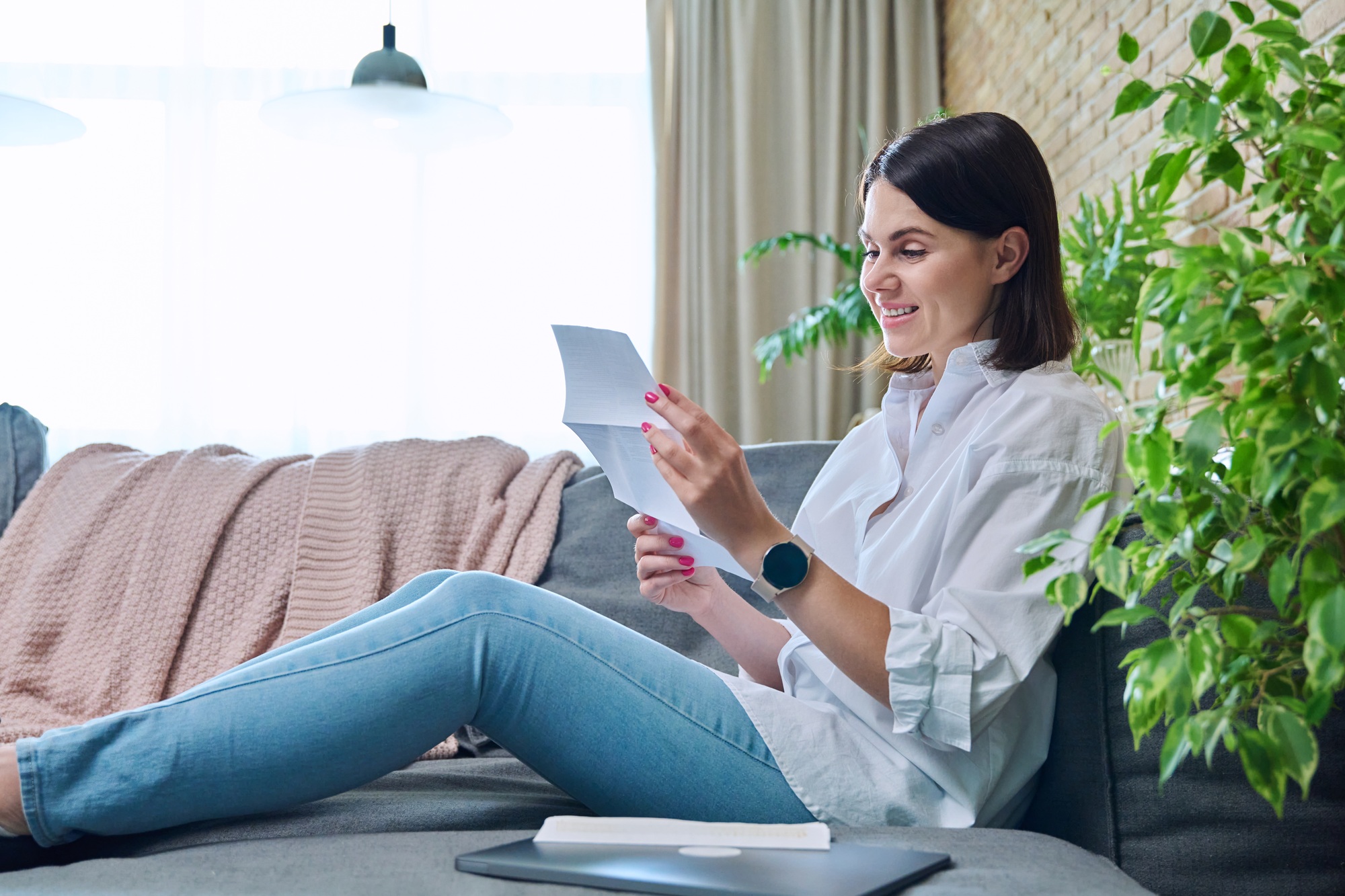Happy young woman reading official paper letter, sitting at home