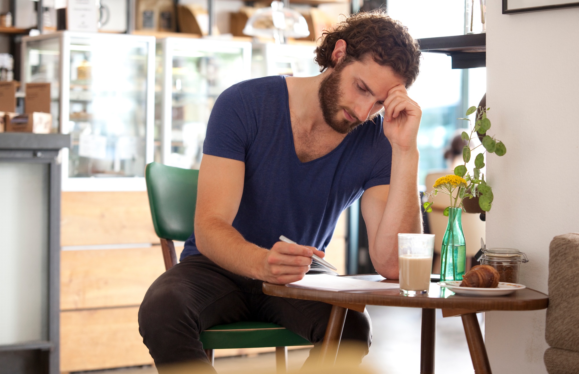Pensive young man sitting in a coffee shop writing letter