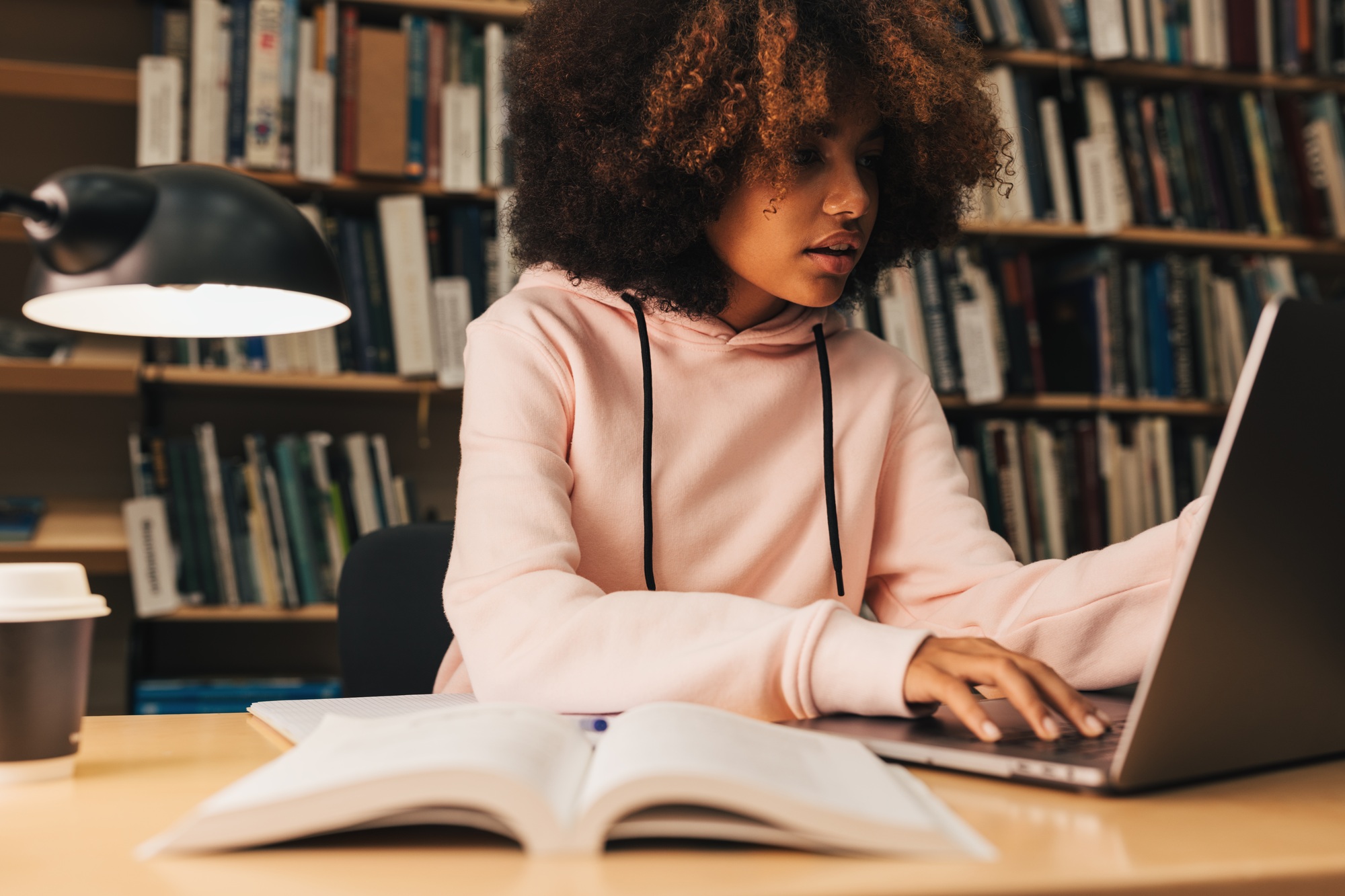 Girl with curly hair typing on laptop in library